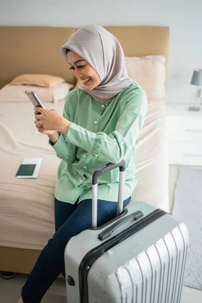 Gesluierde vrouw zat op het bed met haar smartphone en koffer — Stockfoto
