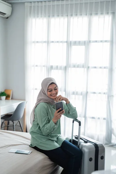 Verschleierte Frau saß mit Smartphone und Koffer auf dem Bett — Stockfoto