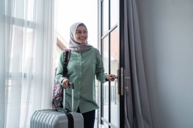 muslim woman traveler opened the door entrance with her bag and suitcase clipart