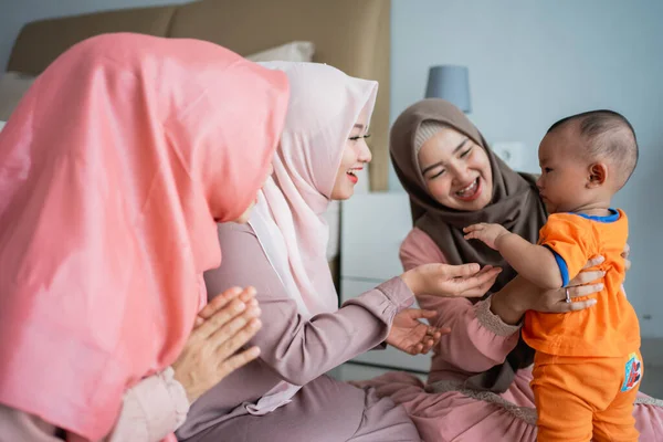 Tiga wanita muslim menikmati bermain dengan anak kecil ketika duduk di lantai — Stok Foto