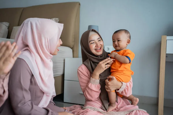 Ibu muslim asia dengan teman-temannya menikmati bermain dengan anaknya ketika duduk di lantai — Stok Foto