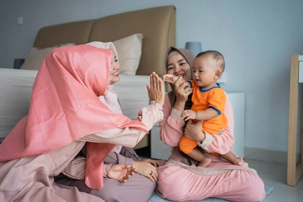 Tiga wanita muslim menikmati bermain dengan anak kecil ketika duduk di lantai — Stok Foto