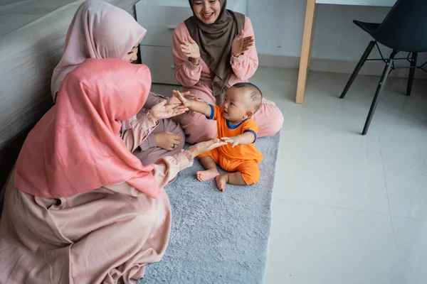 Ibu muslim asia dengan teman-temannya menikmati bermain dengan anaknya ketika duduk di lantai — Stok Foto