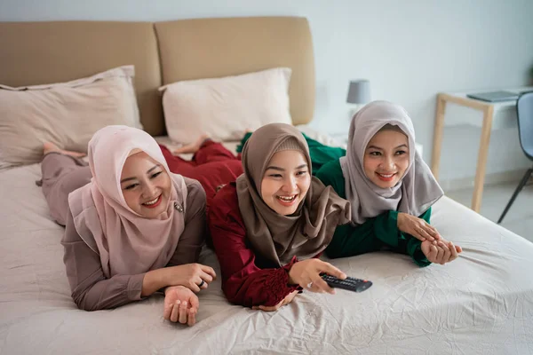 Azji hidżab kobieta z przyjaciółmi leżące na łóżku cieszyć się oglądanie telewizji — Zdjęcie stockowe