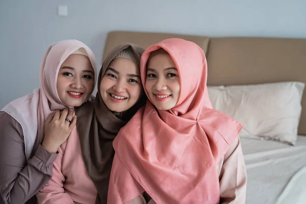 Sonriendo tres mujeres hijab sentadas en la cama en el dormitorio —  Fotos de Stock