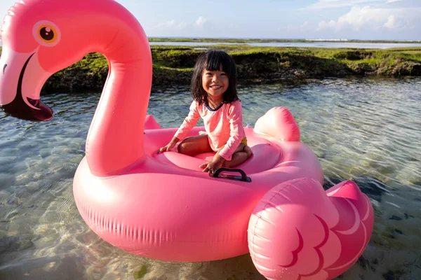 Ένα κοριτσάκι από την Ασία πάνω σε ένα φλαμίνγκο επιπλέει στην παραλία — Φωτογραφία Αρχείου