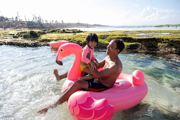 Asiatisk far och dotter rida en flamingo flyter på stranden — Stockfoto