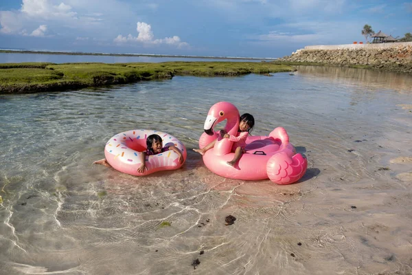 Two little girls enjoying ride on the ring buoy and the flamingo buoy — Stock Photo, Image
