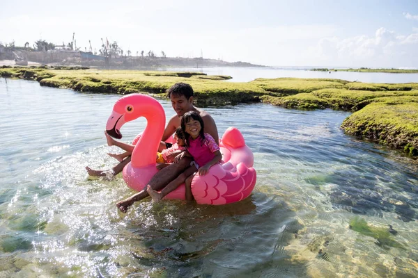 Asijský otec a dvě dcery jezdit plameňák bóje na pláži — Stock fotografie