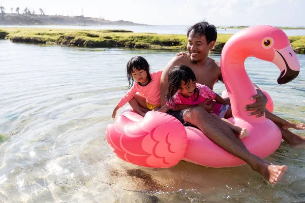 Азиатский отец и две дочери катаются на фламинго-буе по пляжу — стоковое фото