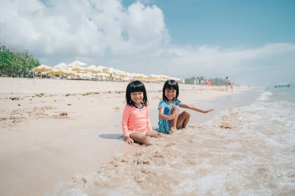 Dos niñas sentadas en la arena esperando que las olas vengan —  Fotos de Stock