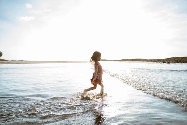 Kleines Mädchen läuft am Strand beim Wasserspielen — Stockfoto