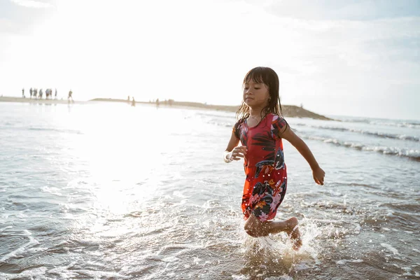 Menina correndo na praia enquanto joga água — Fotografia de Stock