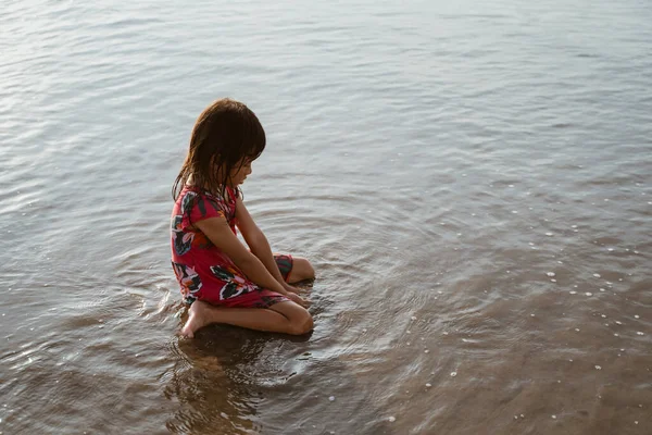 Asiatisch klein mädchen sitting auf sand im die strand während playing water — Stockfoto