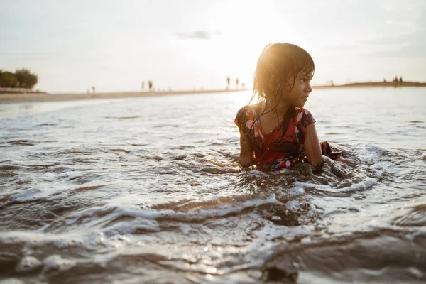 Klein meisje zittend op zand in het strand — Stockfoto
