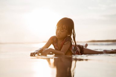 Küçük kız kumsalda suyla oynarken sürünüyor.