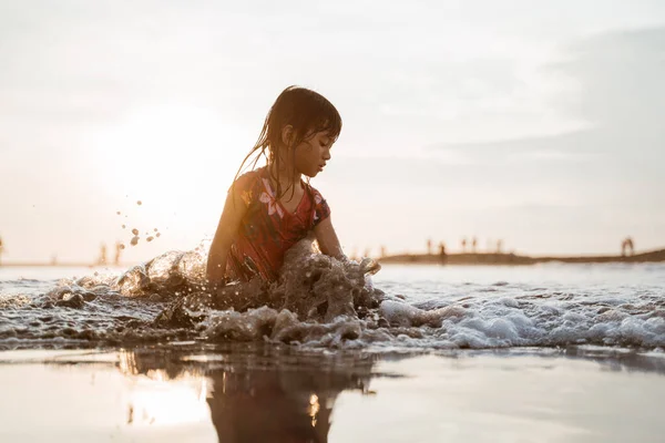 Asiatisch klein mädchen sitting auf sand im die strand während playing water — Stockfoto