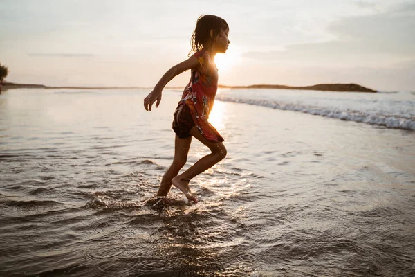 Menina correndo na praia enquanto joga água — Fotografia de Stock