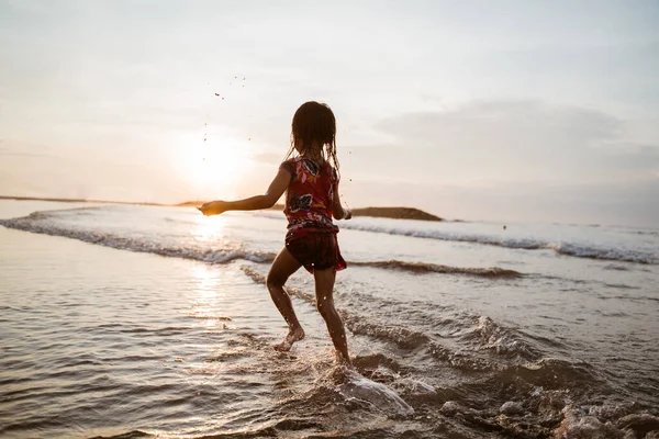 Malá dívka běží na pláži, zatímco hraje vodu — Stock fotografie