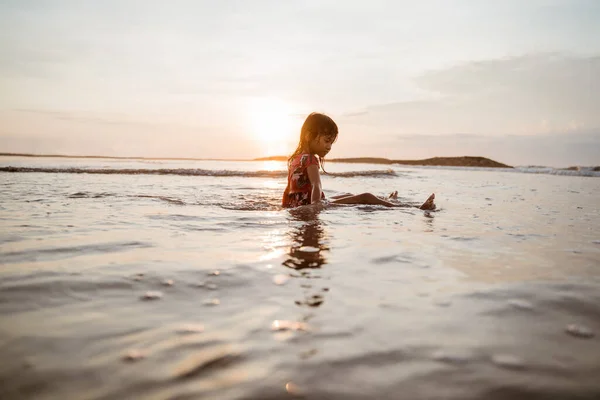 Asiática niña sentada en la arena en la playa mientras juega al agua —  Fotos de Stock