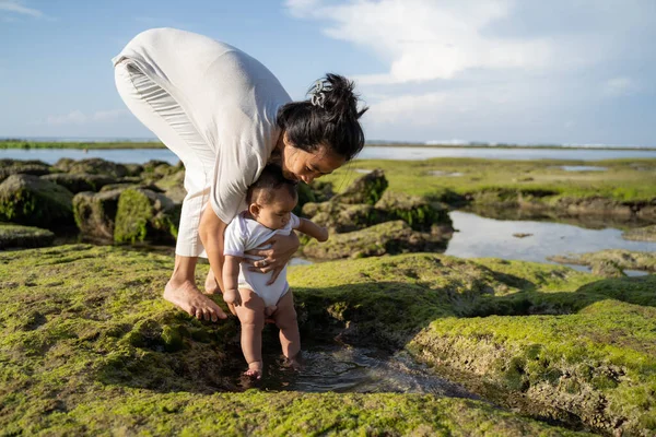 Mãe segura o bebê quando os pés dos bebês são tocados na praia de areia — Fotografia de Stock