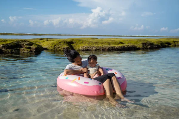 Aziatische moeder en baby rijden de rubberen ring drijven op het strand — Stockfoto