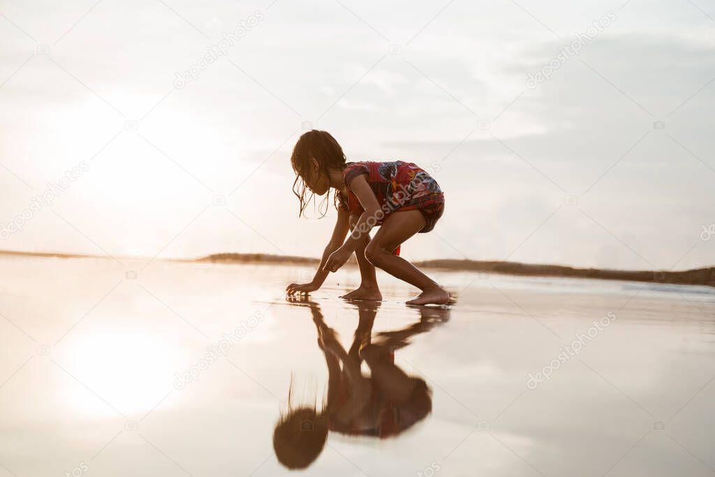 little girl bent over and playing sand on the beach