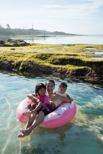 Asyalı anne ve iki çocuğu şamandıra halkasına binerken gülüyorlar. — Stok fotoğraf
