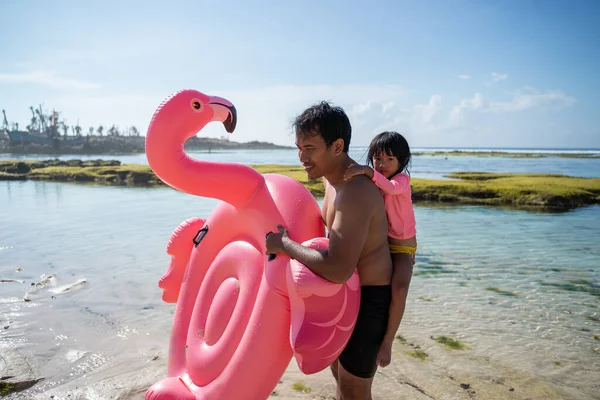 Pai dando piggyback seu filho enquanto carrega uma bóia flamingo — Fotografia de Stock