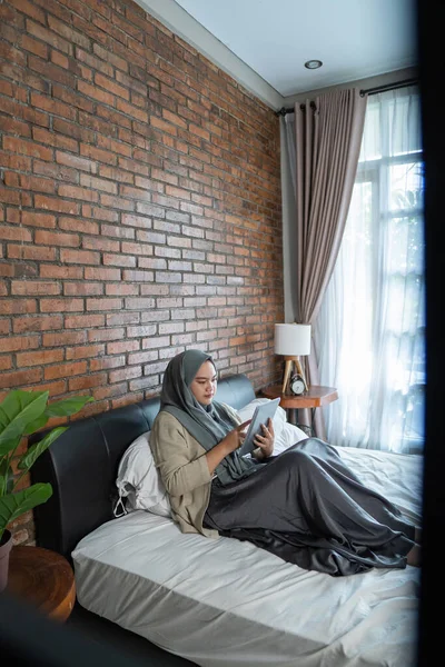 Мусульманская азиатка с помощью планшета сидит на кровати — стоковое фото