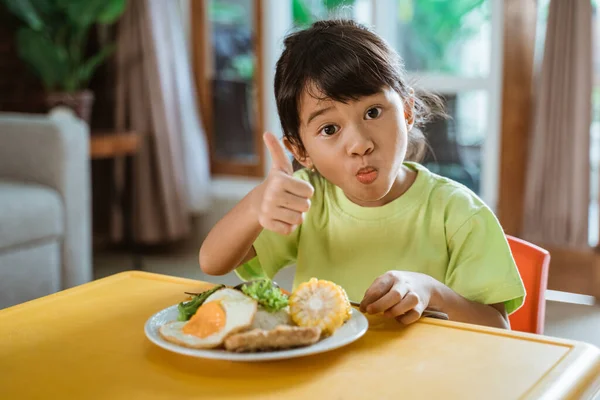 Kid showing thumb up while having breakfast — Stock Photo, Image