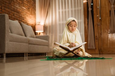 Kız evde tek başına Kuran okuyor.