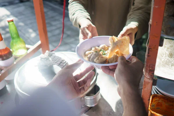 Street food verkoper overhandigt een kom bakso — Stockfoto