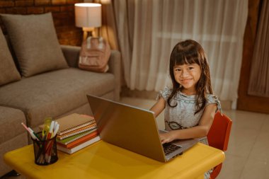 Mutlu küçük kız ödevlerini yaparken dizüstü bilgisayar kullanıyor.