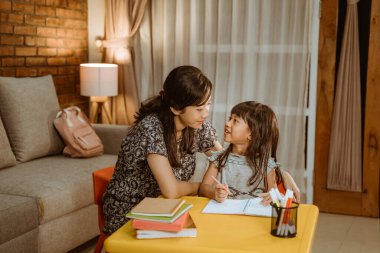 Anne kızının çalışmasına yardım ediyor.