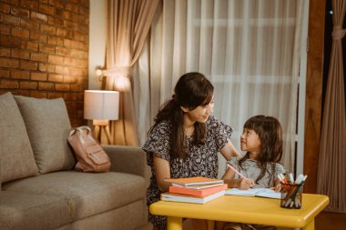 Anne kızının çalışmasına yardım ediyor.