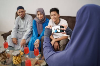 Erkek müslüman, kanepede otururken ailesinin fotoğrafını çekiyor.