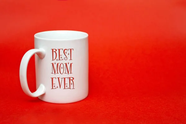 White mug with sign  Best mom ever on red background. Copy space for writing. White glass isolated. International women\'s day concept.  March 8 concept