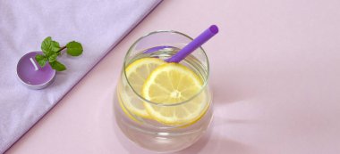 Bir bardak su, limon, nane ve mum. Bardak saf su ve taze organik limon ve nane mor arka plan ve mor mum izole. Detoks ve sağlıklı gıda kavramı