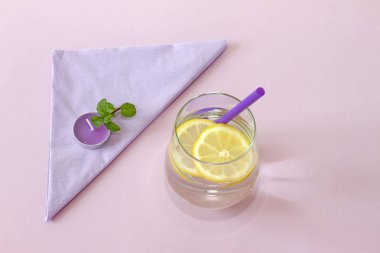 Bir bardak su, limon, nane ve mum. Bardak saf su ve taze organik limon ve nane mor arka plan ve mor mum izole. Detoks ve sağlıklı gıda kavramı