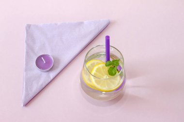 Bir bardak su, limon, nane ve mum. Bardak saf su ve taze organik limon ve nane mor arka plan ve mor mum izole. Detoks ve sağlıklı gıda kavramı