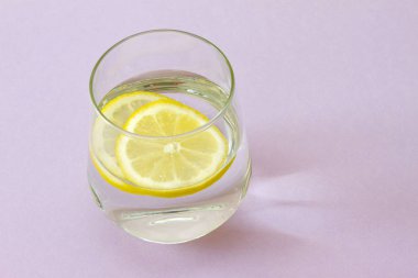 Bir bardak su ve limon. Bardak saf su ve taze organik limon mor arka plan üzerinde izole. Detoks ve sağlıklı gıda kavramı. Senin metabolizma kavramı artırmak. 