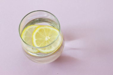 Bir bardak su ve limon. Bardak saf su ve taze organik limon mor arka plan üzerinde izole. Detoks ve sağlıklı gıda kavramı. Senin metabolizma kavramı artırmak. 
