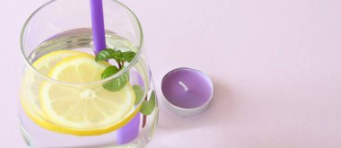 Bir bardak su, limon, nane ve mum. Bardak saf su ve taze organik limon ve nane mor arka plan ve mor mum izole. Detoks ve sağlıklı gıda kavramı