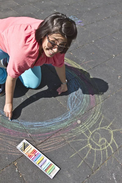 Young woman draw with color chalks on a street. Fun and having good time concept. Vacation and break time. Woman Teacher draw in the yard. Kinder garden or preschool teacher. Anti stress concept.