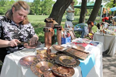 Bir kadın çekiç bakır plakalar ve hediyelik eşyalarla iş yapıyor.