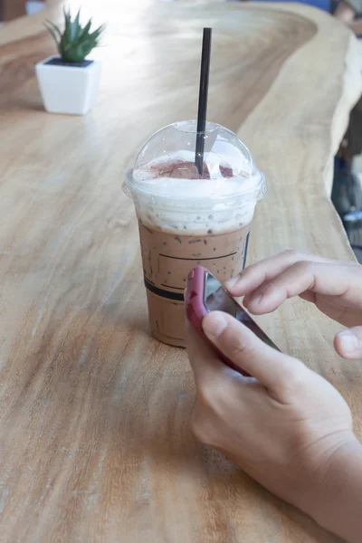 Mujer mano sosteniendo el teléfono con fondo de café helado — Foto de Stock