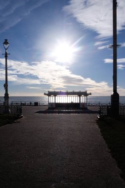Brighton seafront, gökyüzünde düşük ve dramatik bir mavi ve beyaz bulutlu gökyüzü şekillendirme, aydınlatma oturma barınak içine parlayan bir oturma barınak, güneşin önde gelen ön planda mesire.