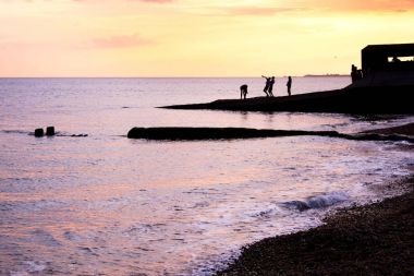 Brighton Plajı deniz günbatımı iskele, iskeleye silhoutted tarafından parlak turuncu siyah olduğunu ve günbatımı, iskele üzerinde sarı kızdırma iskelede oynarken teanagers bir grup, onlar güneş tarafından silhoutted çok hareketli siyah insan şekilleri vardır.