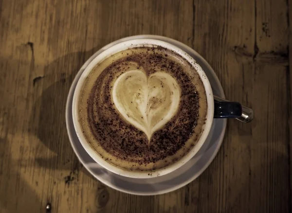 Cup of coffee with heart shape in it. made out of froth, wooden — Stock Photo, Image